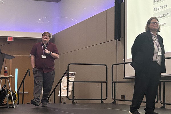 2 people on stage. one is holding a microphone, walking and smiling.