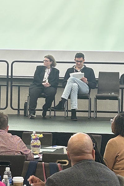 2 people sitting on stage. 3 people sitting down in the foreground.