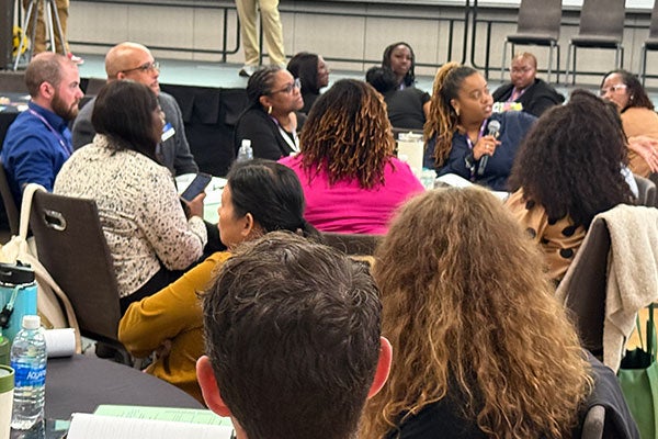 People sitting down at an event. One person is holding a microphone.